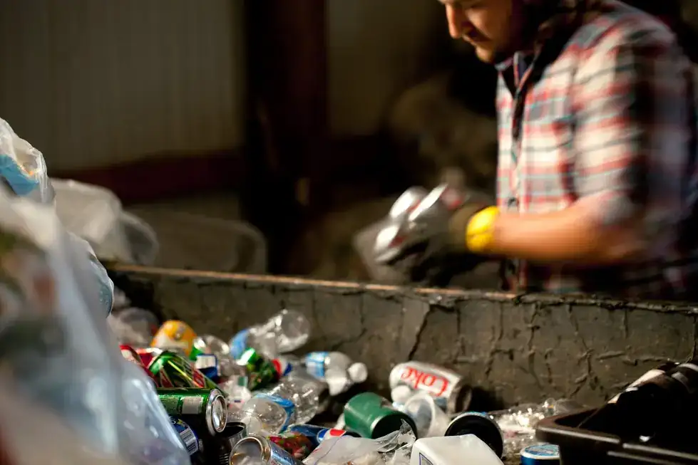 A worker in a yellow glove sorting cans and bottles on the sort line