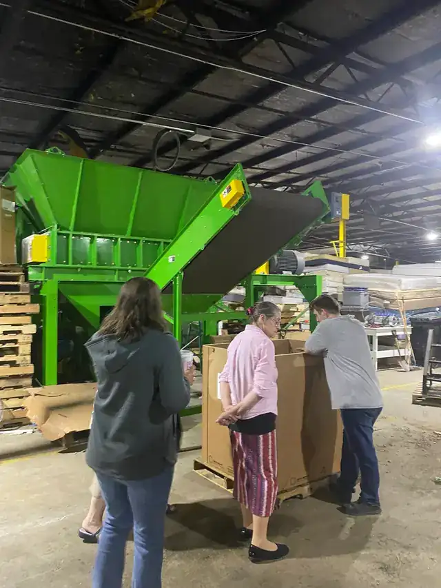 Visitors on a tour beside the green mattress shredder