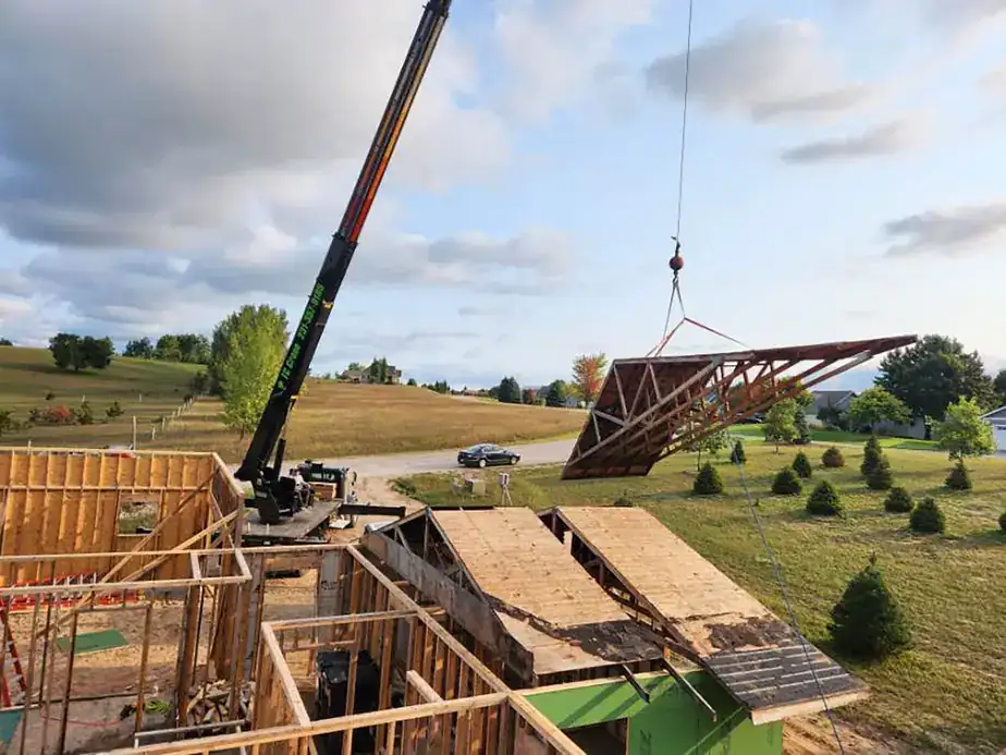 A crane lifting a roof truss off a house frame